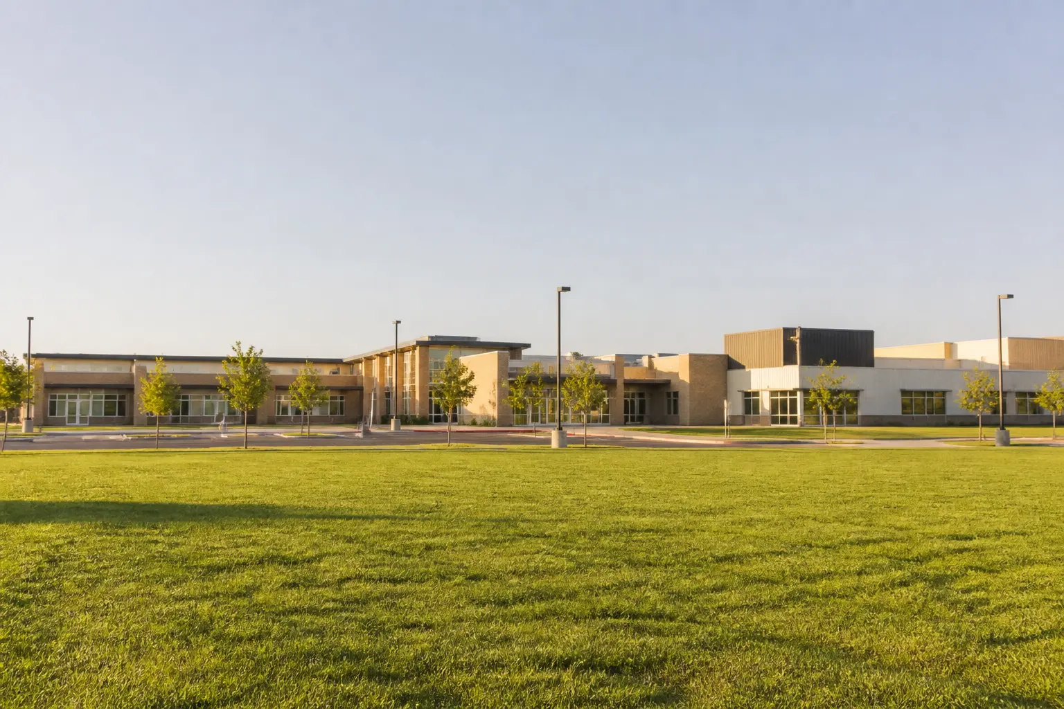 A modern single-story school building set behind a wide open lawn under a clear sky.