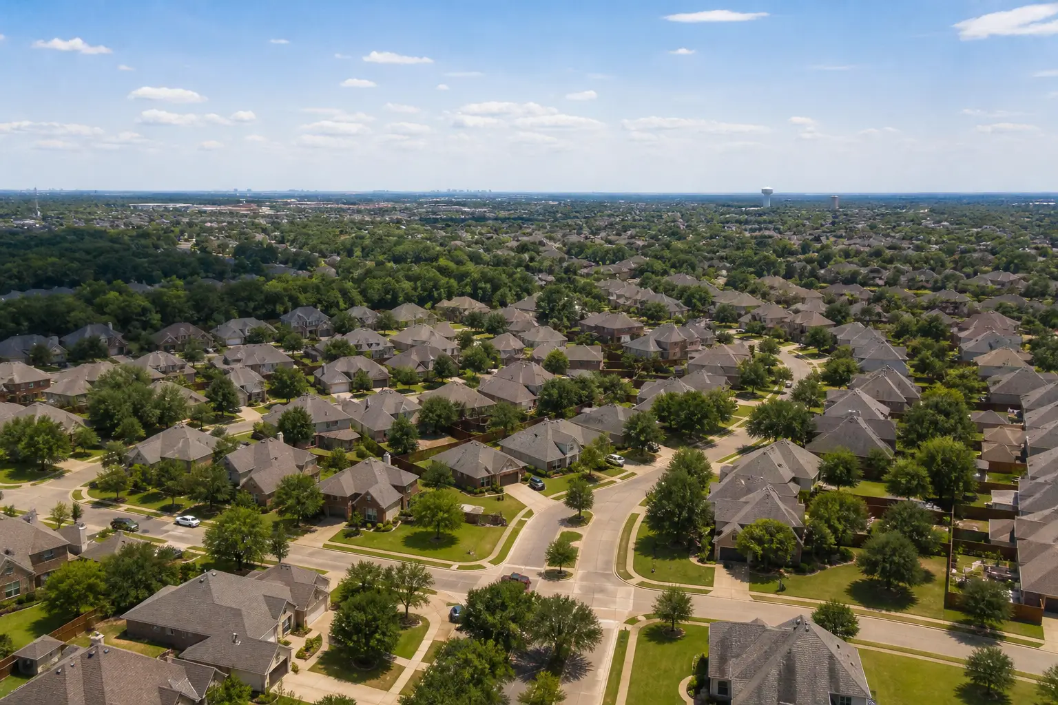 An aerial view of a tree-lined suburban neighborhood with a skyline far in the distance.