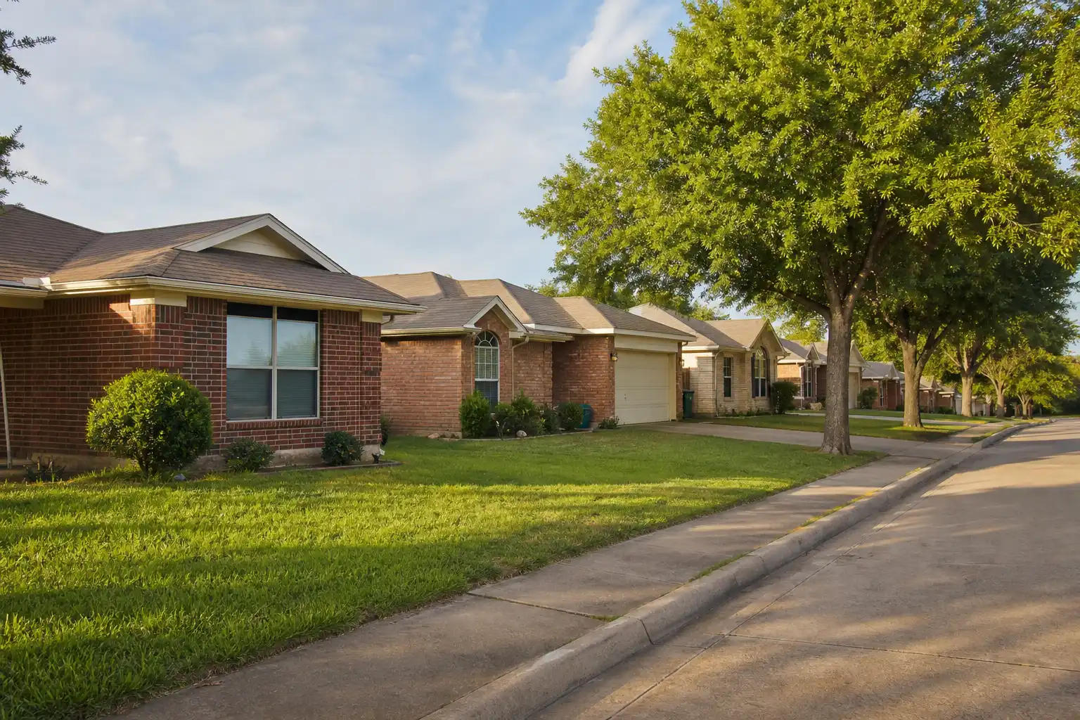 A street of single-story brick homes with mature shade trees and front lawns.