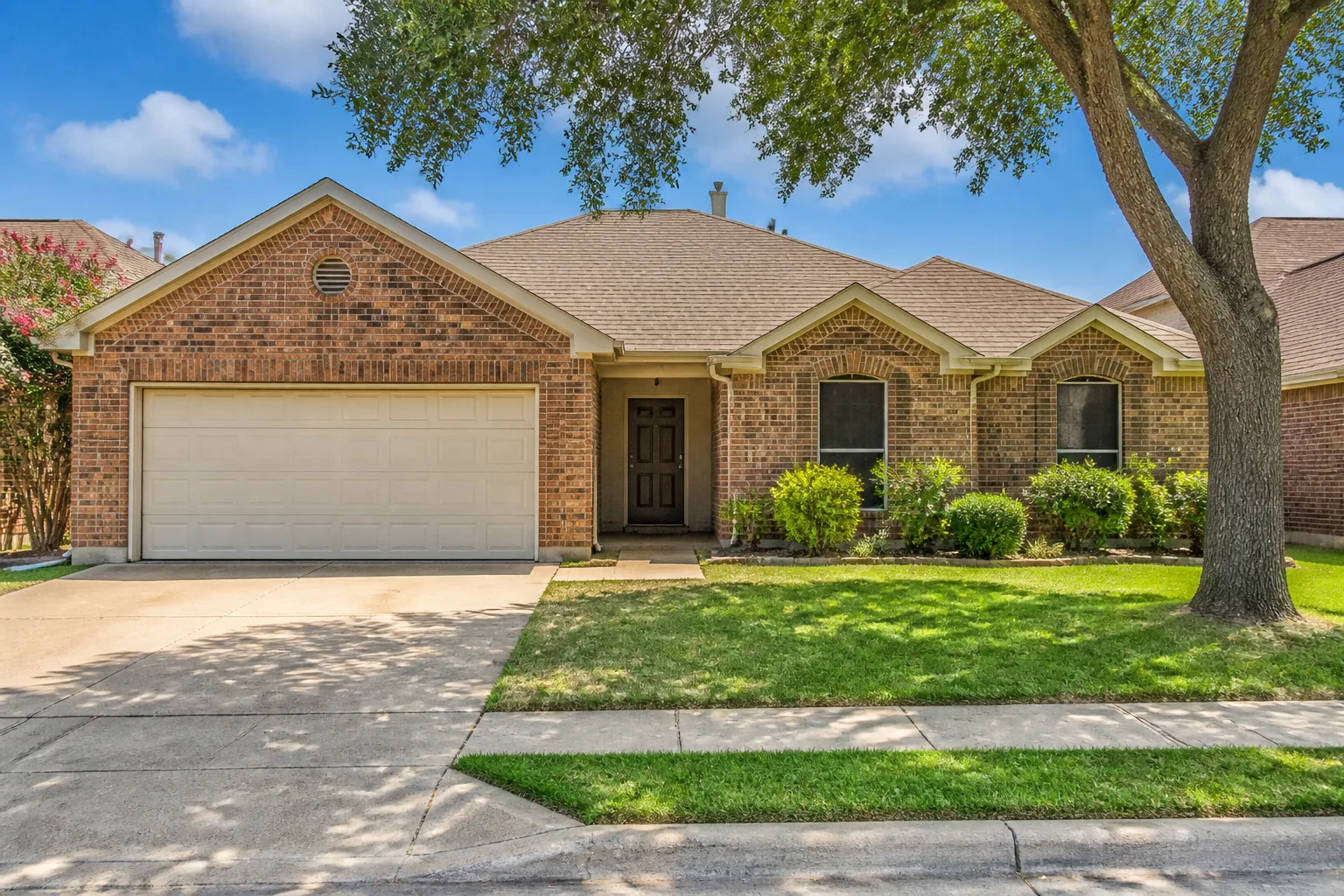 The front of a single-story brick suburban house with a two-car garage and a green lawn.
