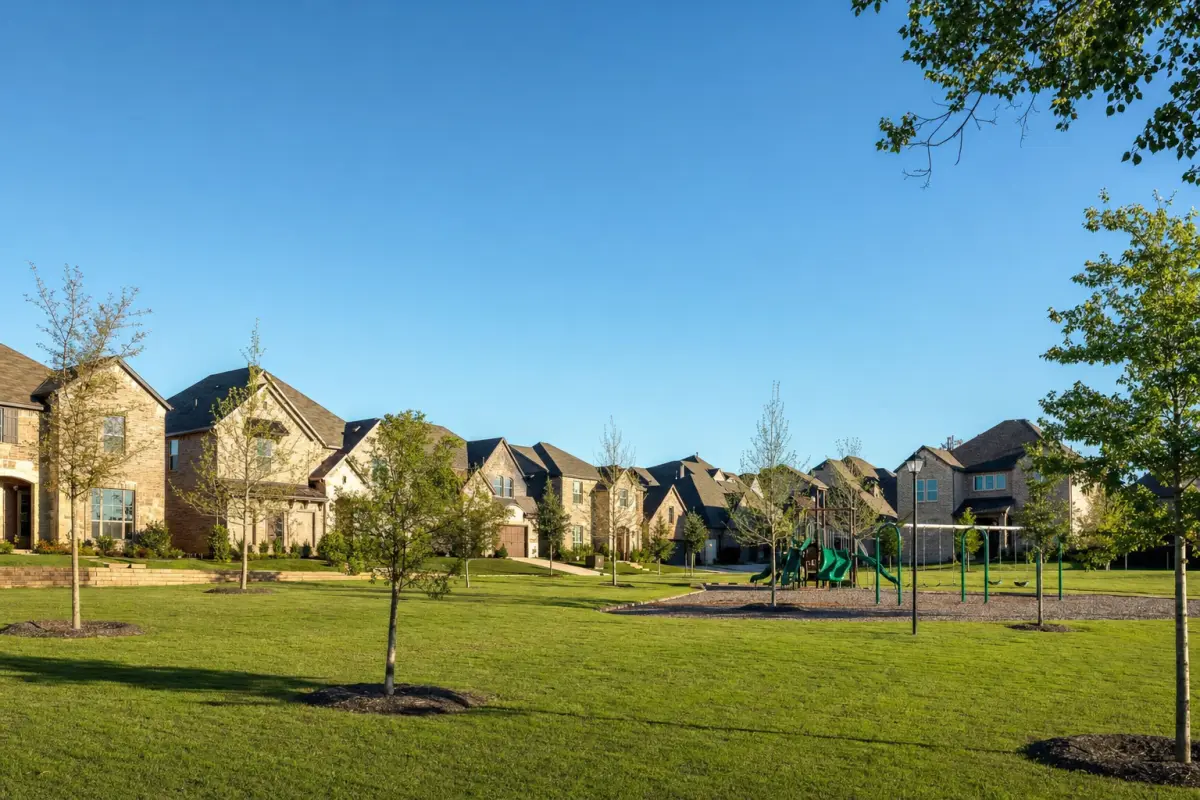 Newly built brick homes seen across a grassy neighborhood green with a playground.