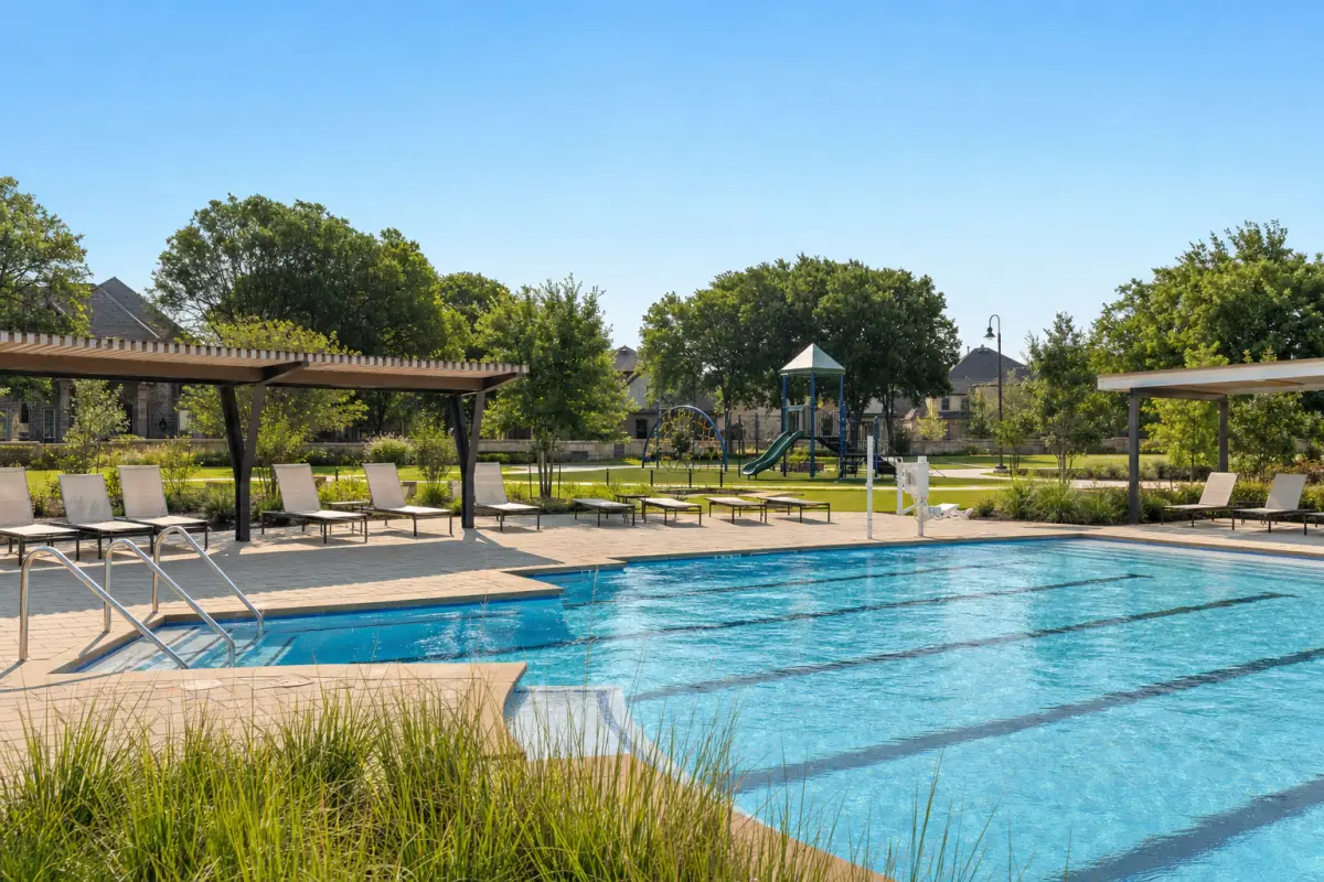 A neighborhood pool deck with shade structures, a playground and an open lawn behind it.