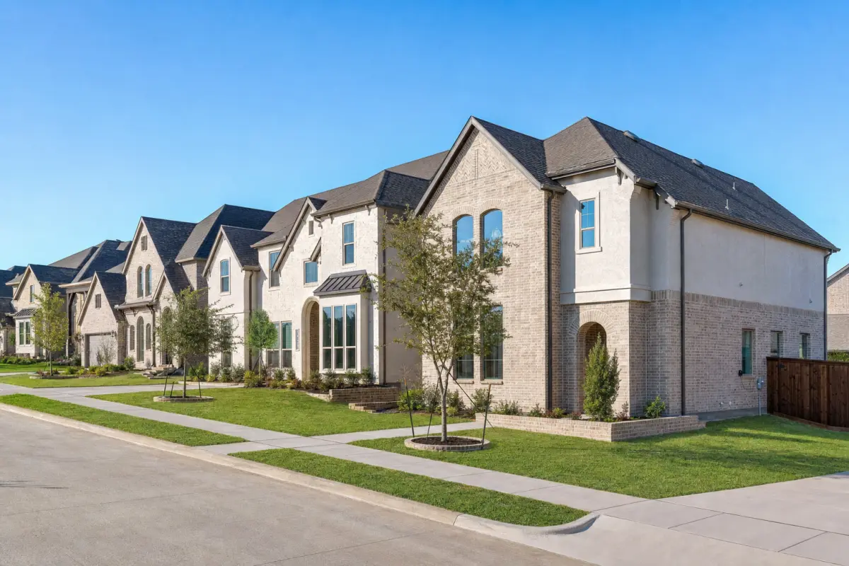 A row of newly built two-story homes with young trees along a new concrete street.