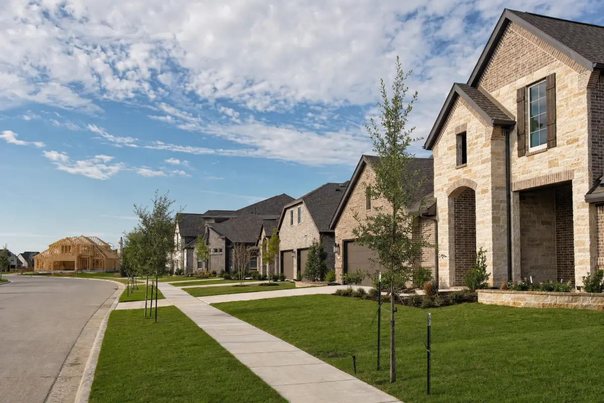 A street of newly built brick homes with young trees and one house still under construction.