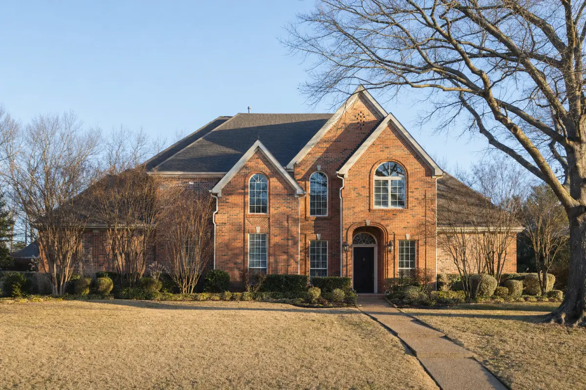 A two-story brick house with a front lawn and bare trees on a clear winter morning.