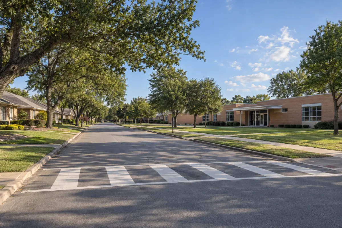 A quiet residential street with brick homes on one side and a low brick building behind a lawn on the other.